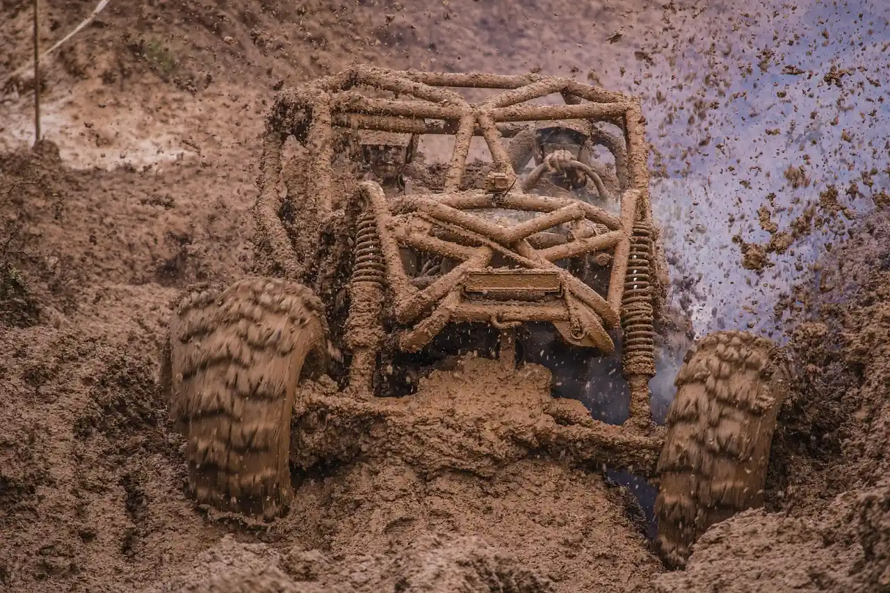 Mud-caked off-road buggy digging through a rut with a tire clawing for grip
