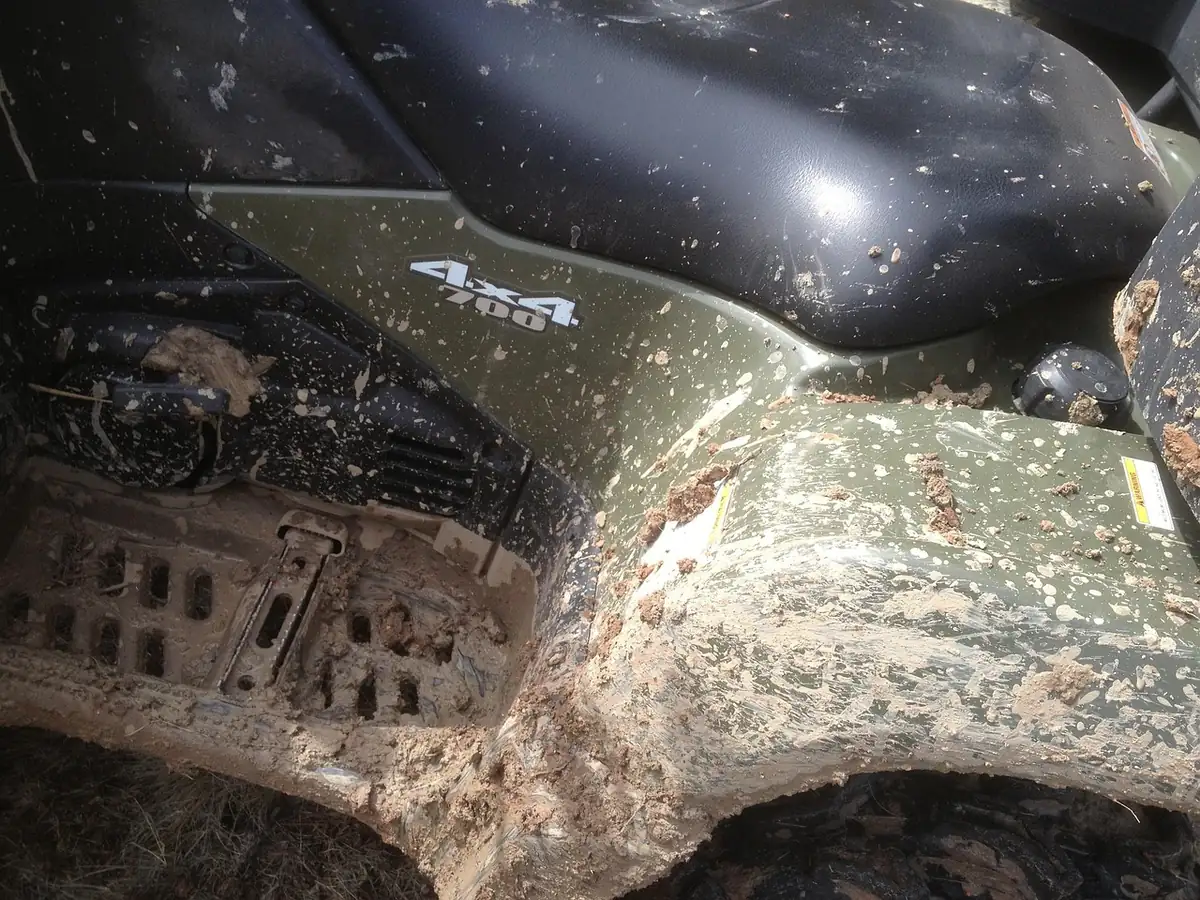 Mud-caked green ATV fender and lower body panels after a muddy ride