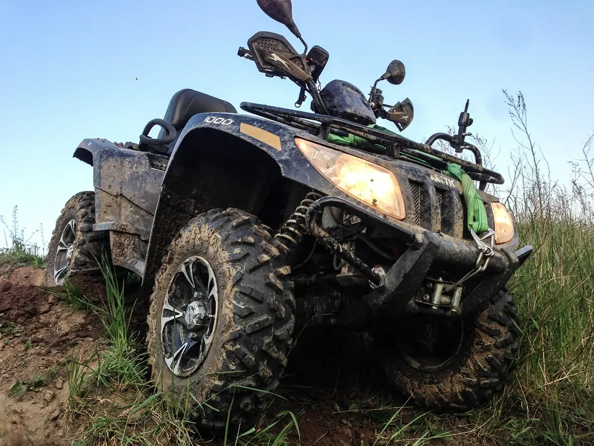Mud-splattered ATV tilted on a grassy hillside with the front fender and rack visible