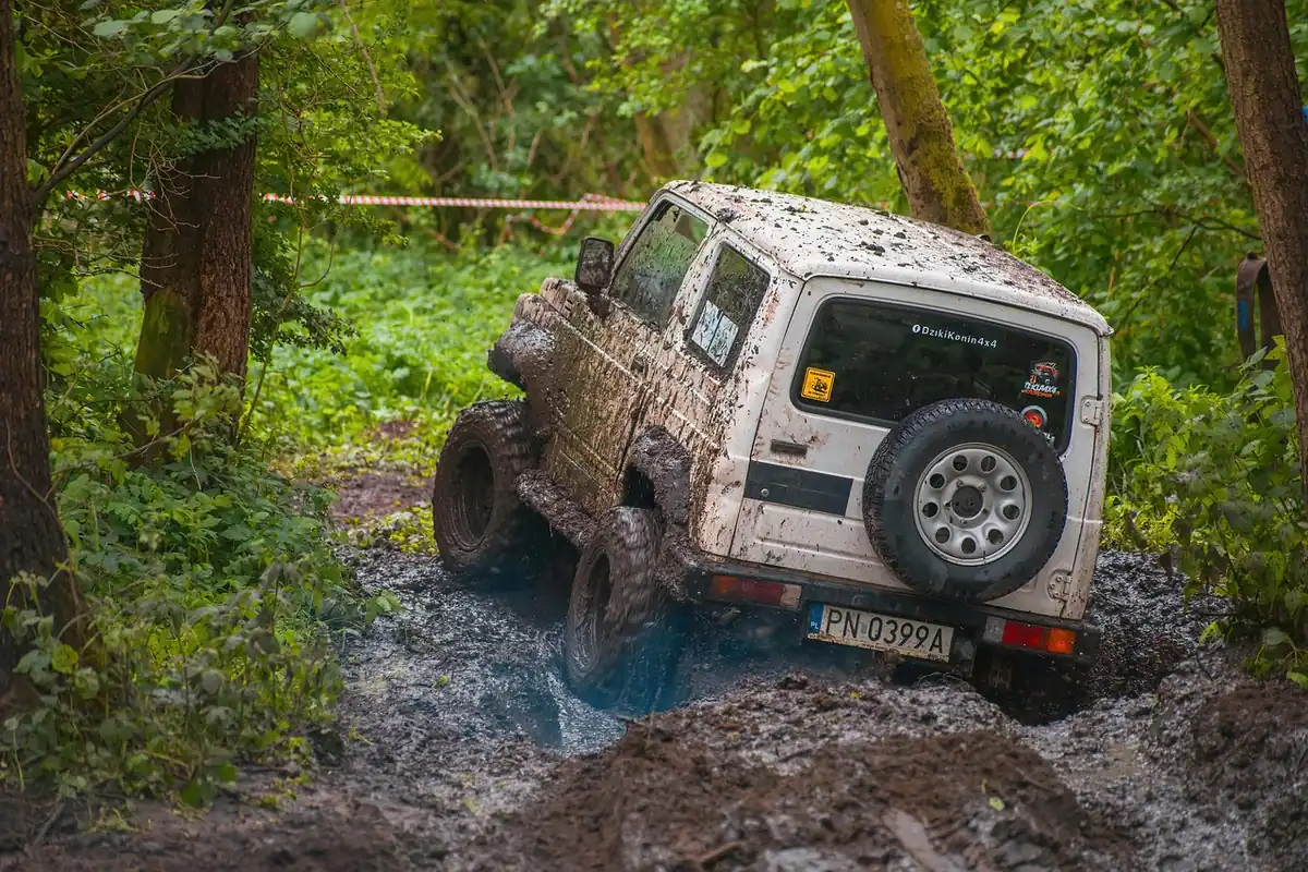 Muddy SUV with off-road tires climbing out of a mud pit on a wooded trail