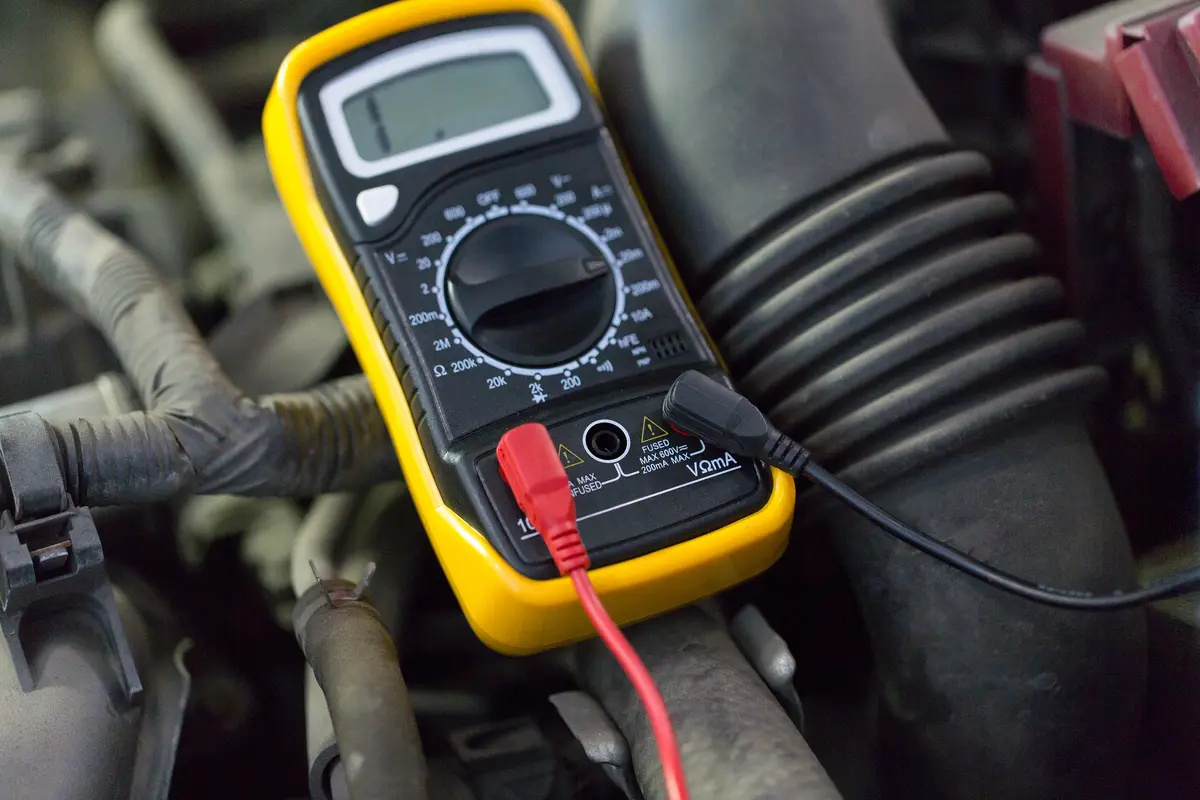 Digital multimeter with red and black test leads checking voltage under a hood