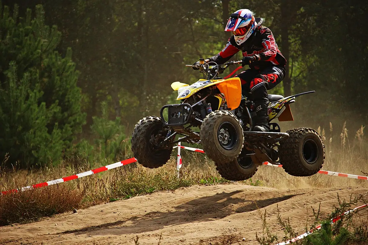 ATV rider in a full-face helmet airborne over a dirt hill on a marked course