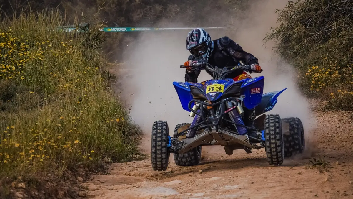 Rider on a blue quad ATV kicking up dust on a dirt trail