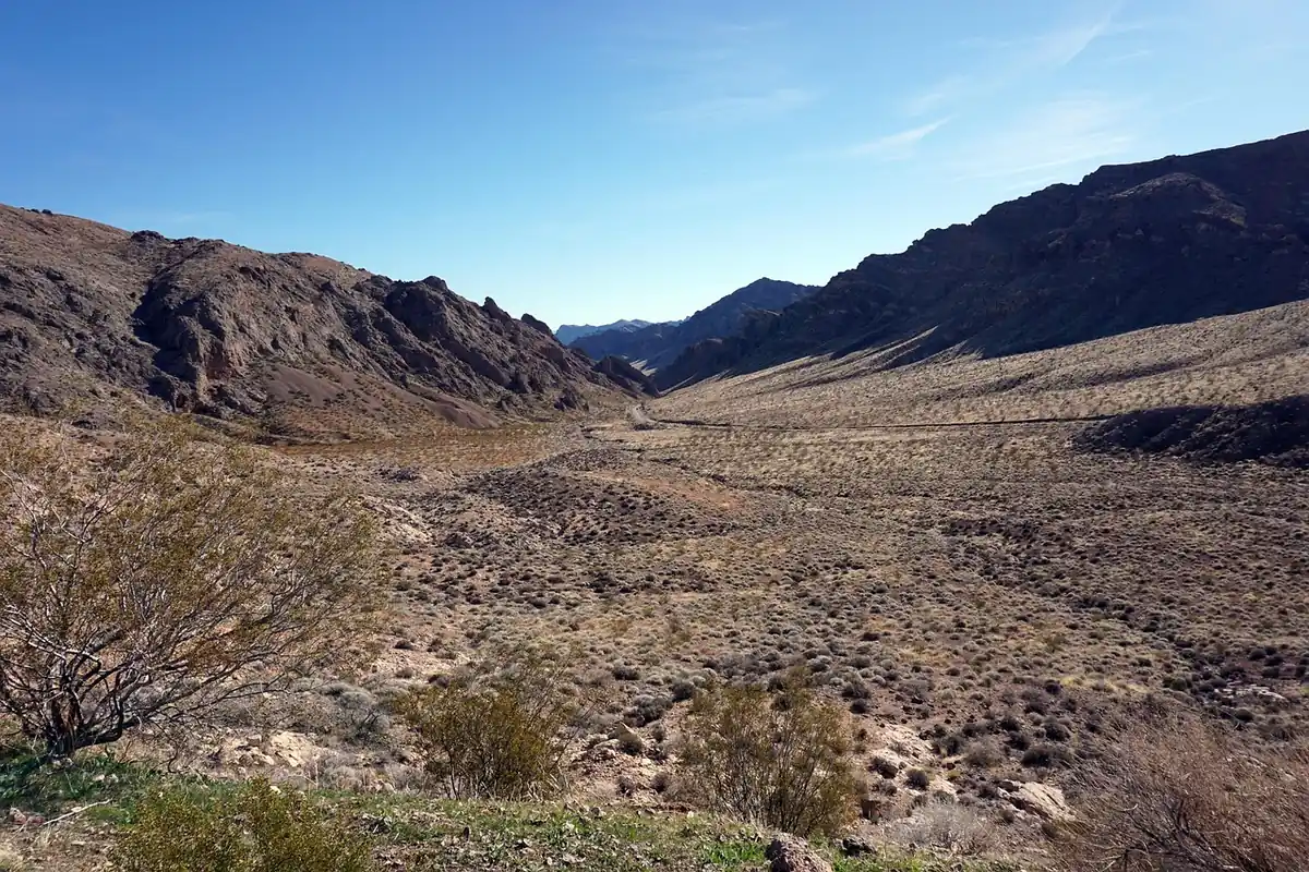 A dirt track running through a wide Nevada desert valley between dark mountain ridges