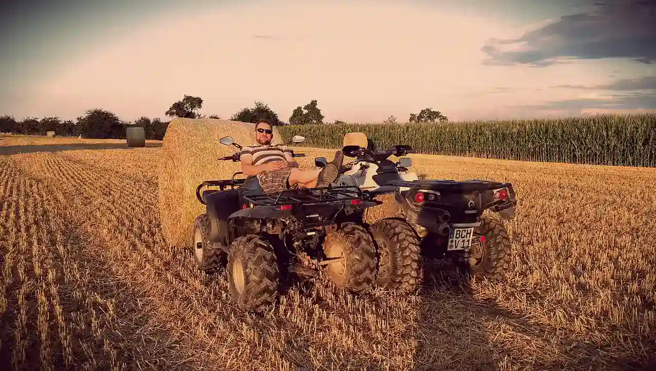 Two quad bikes parked on a harvested field beside a hay bale at sunset