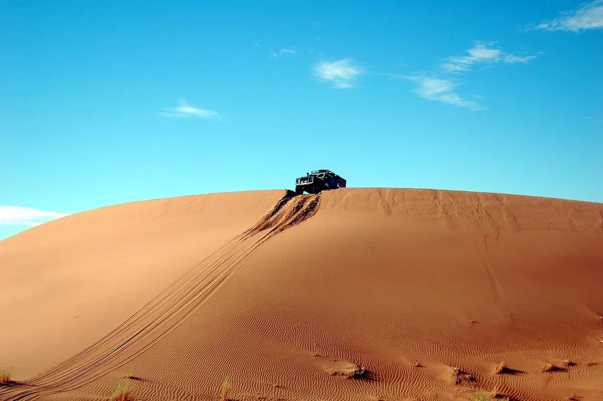 Four-wheel-drive vehicle at the crest of a large sand dune with tire tracks leading up the slope