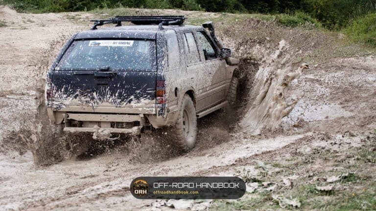 Older 4x4 SUV with a roof rack and snorkel splashing through a muddy off-road trail