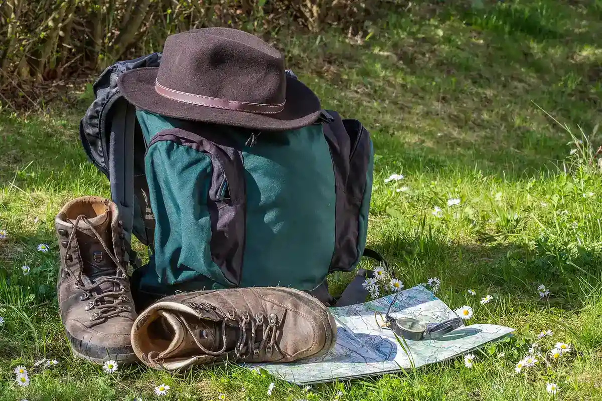 Paper trail map, hiking boots and a backpack on grass