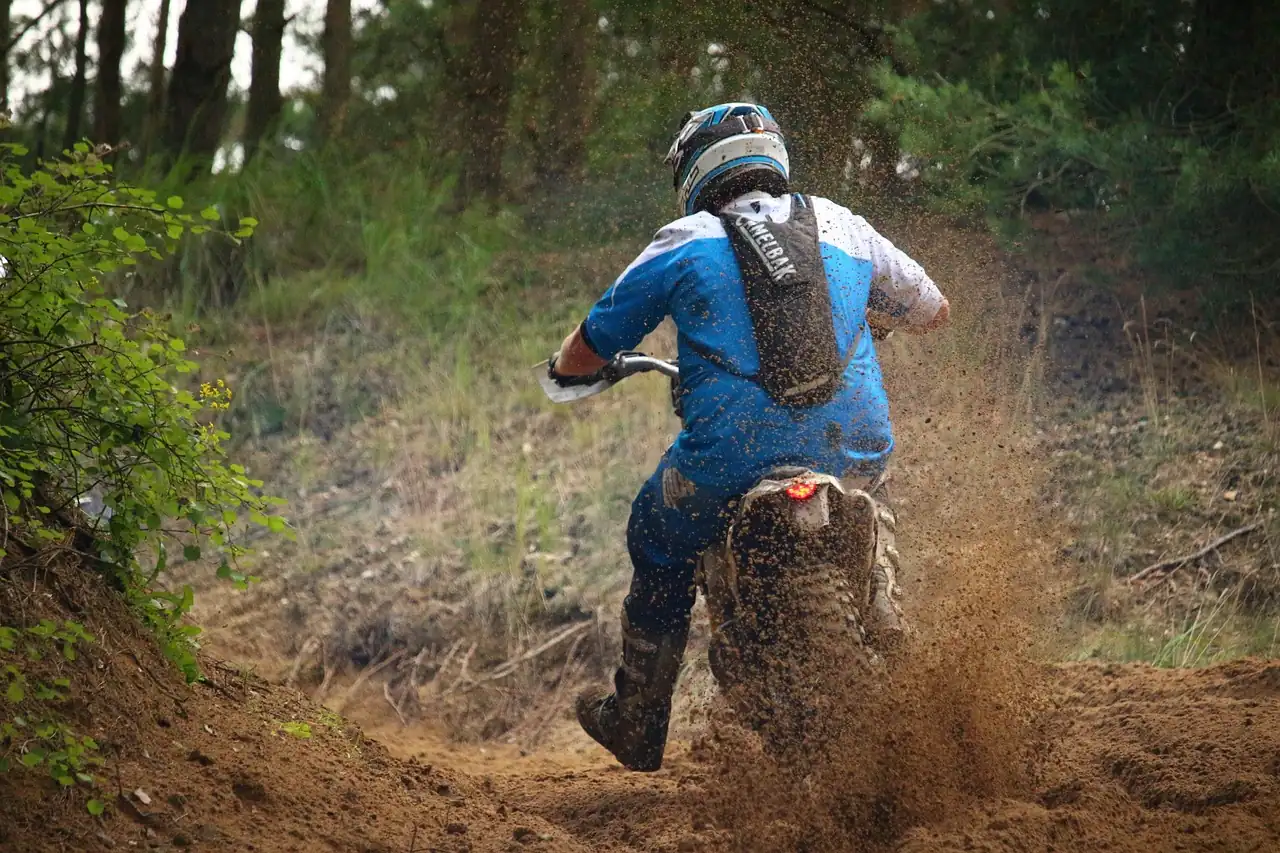 Dirt bike rider in a helmet and backpack throwing mud on a wooded trail