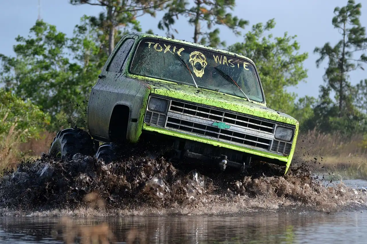 Lifted green pickup truck with big tires plowing through a deep mud pit