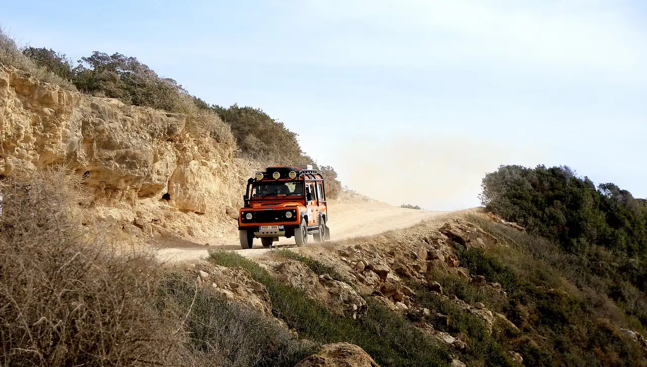 Orange 4x4 driving along a dusty dirt road on a cliffside