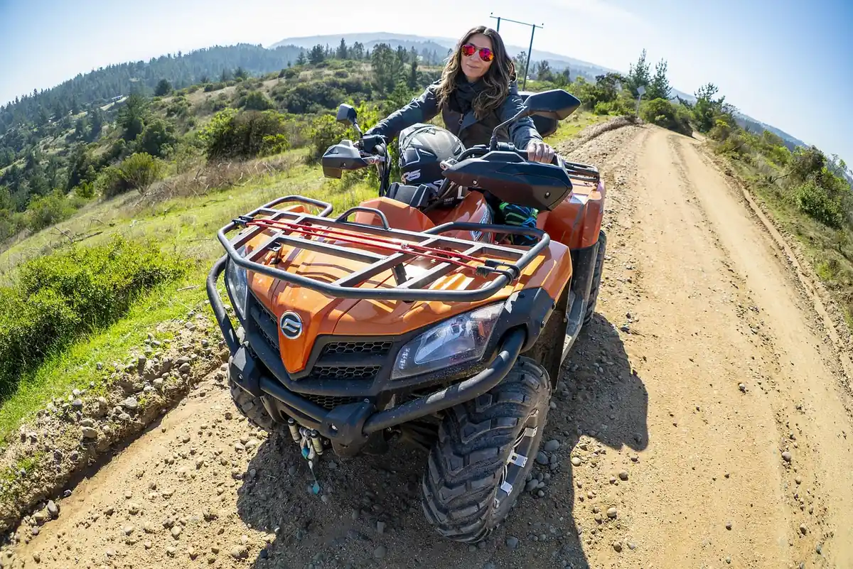 Rider on an orange utility ATV with a front rack on a dirt road along a hillside