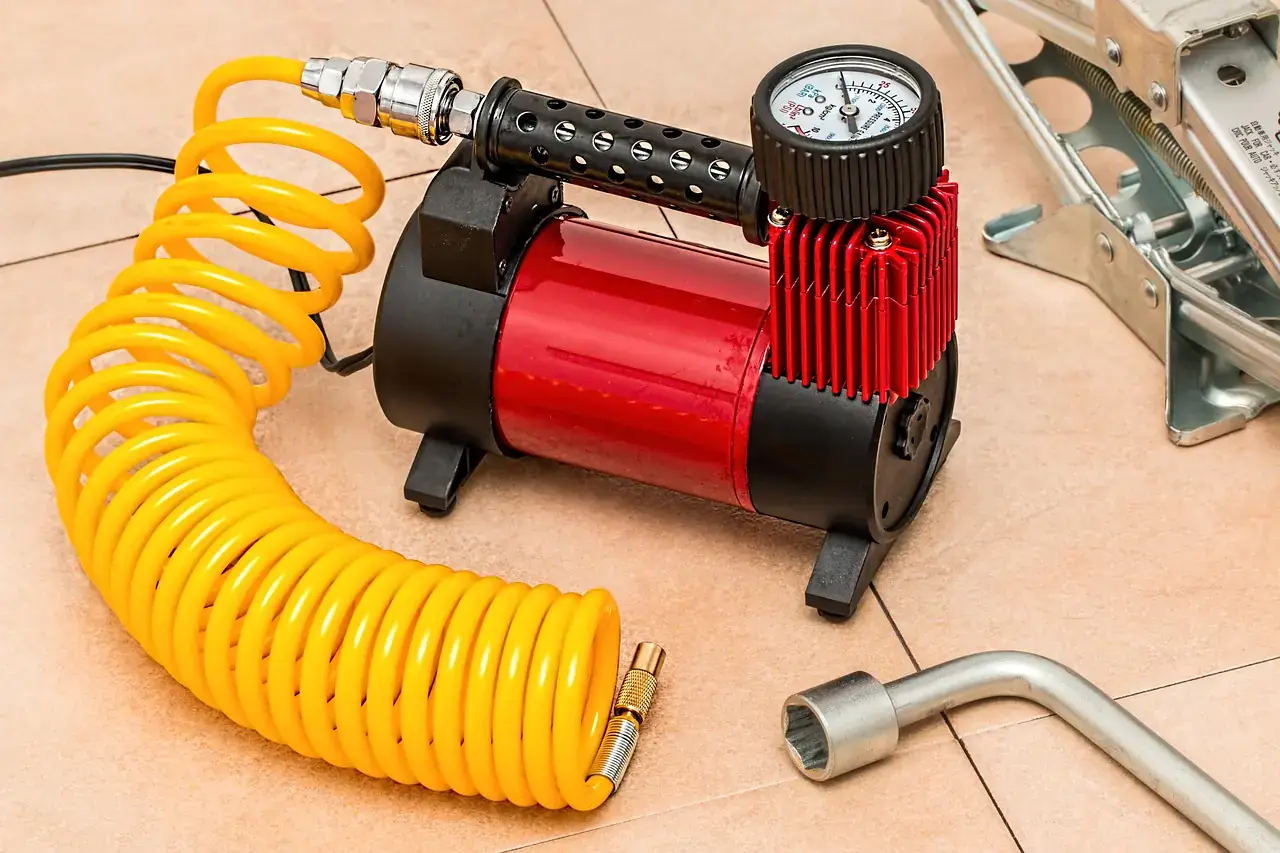 Portable 12-volt air compressor with a yellow coiled hose and pressure gauge next to a lug wrench