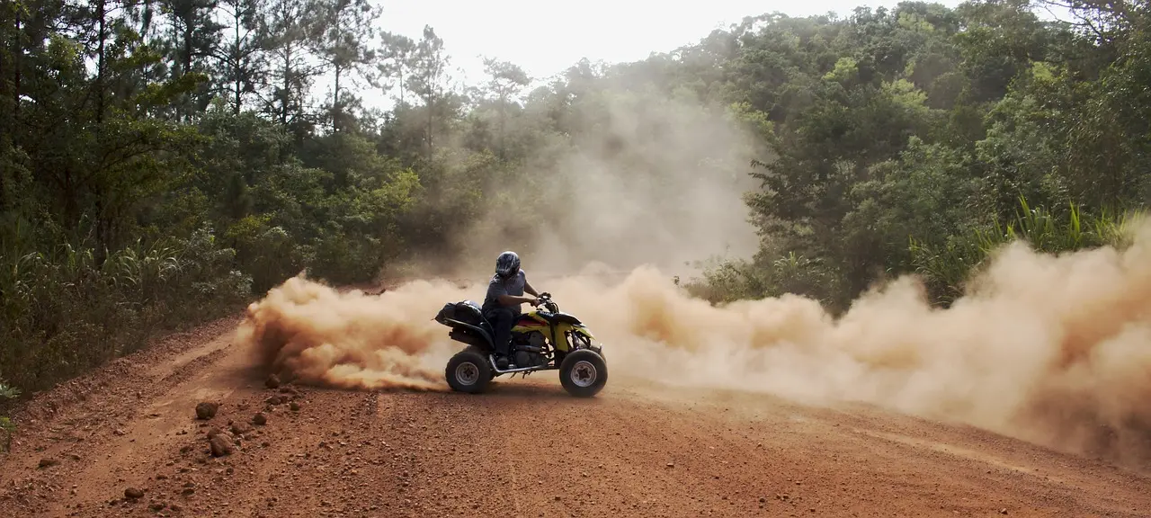Rider on a yellow and black ATV sliding through a cloud of red dust on a forest dirt road