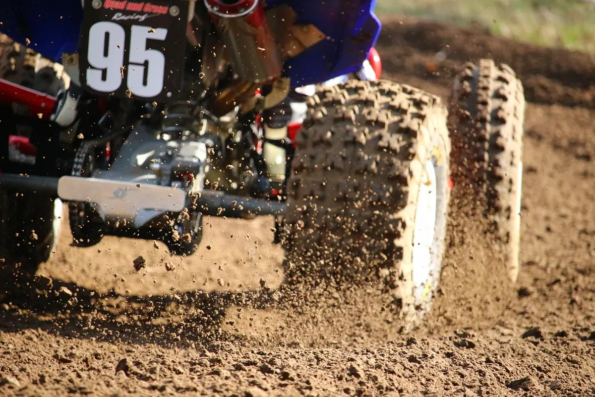 Close view of a quad bike rear tire and wheel throwing dirt on a track