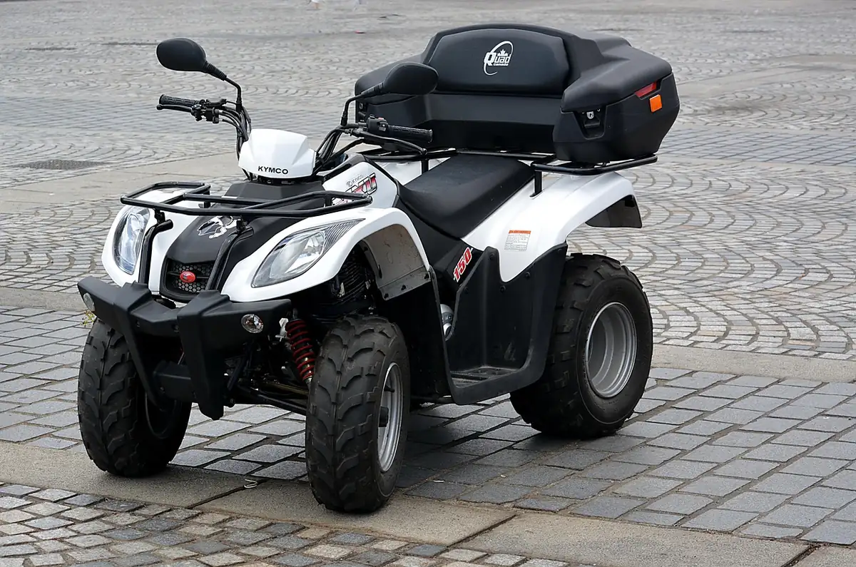 White and black utility quad with a rear storage box parked on cobblestone pavement