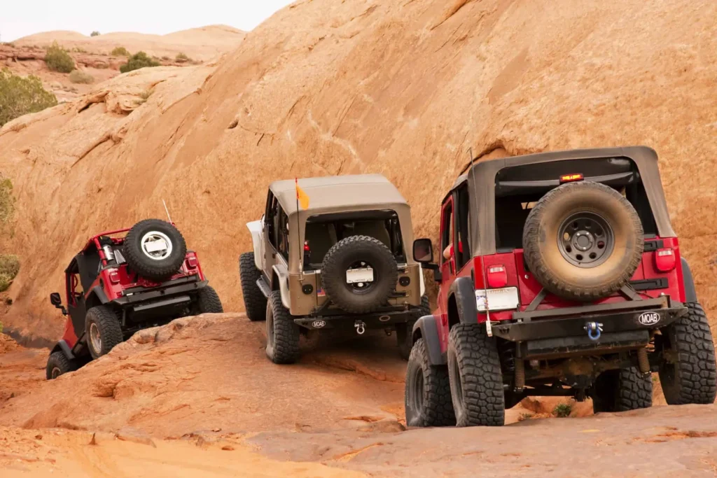 Three Jeep Wranglers crawling up a red slickrock trail
