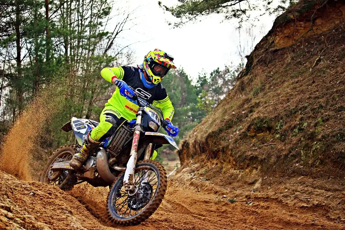 Dirt bike rider leaning through a sandy berm on a wooded trail