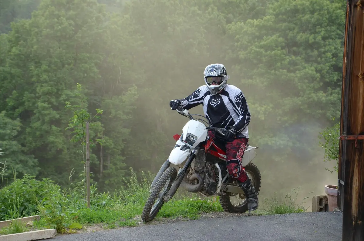 Rider in helmet, goggles and protective gear on a dirt bike with dust and trees behind