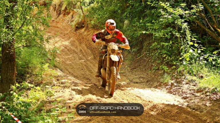 Dirt bike rider coming down a sandy wooded trail with trees on both sides
