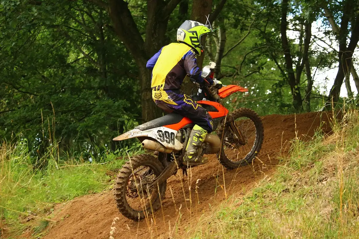 Dirt bike rider climbing a grassy hill trail between trees