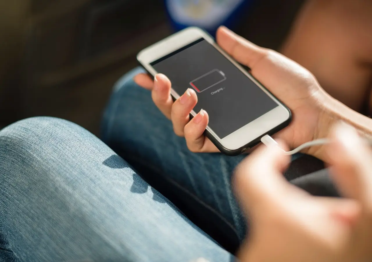 Hand plugging a charging cable into a phone with a low battery screen