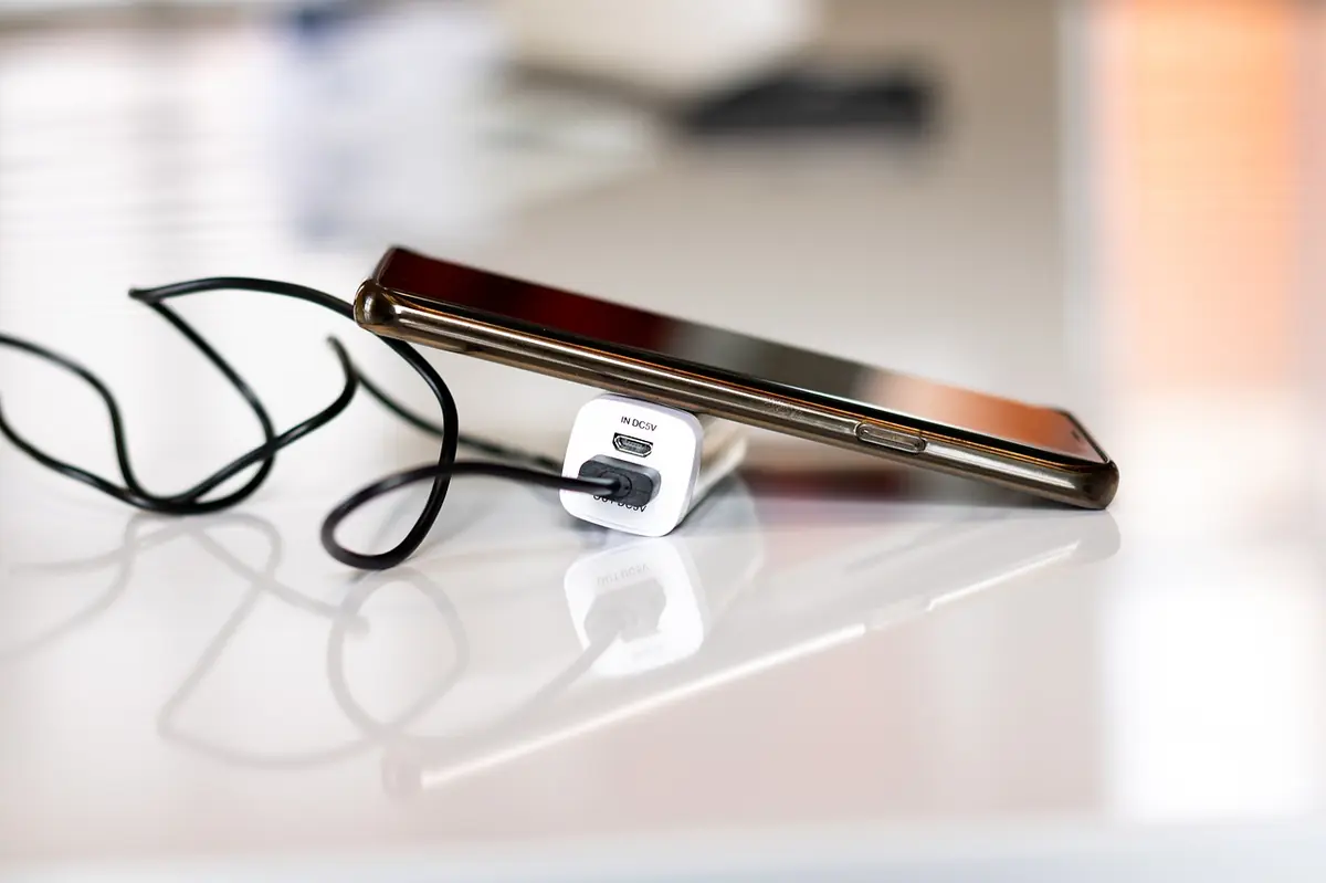 Smartphone lying on a white surface charging from a USB adapter and cable