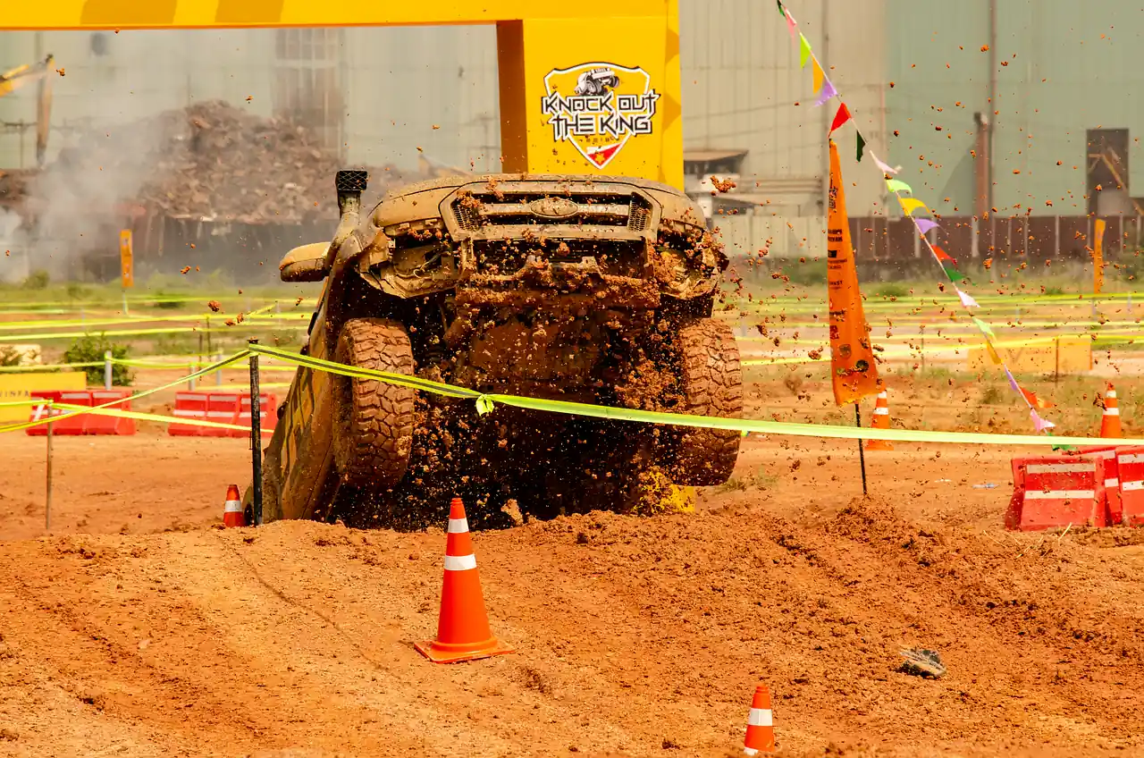 Four-wheel-drive pickup truck driving through mud and red dirt on an off-road course with traffic cones