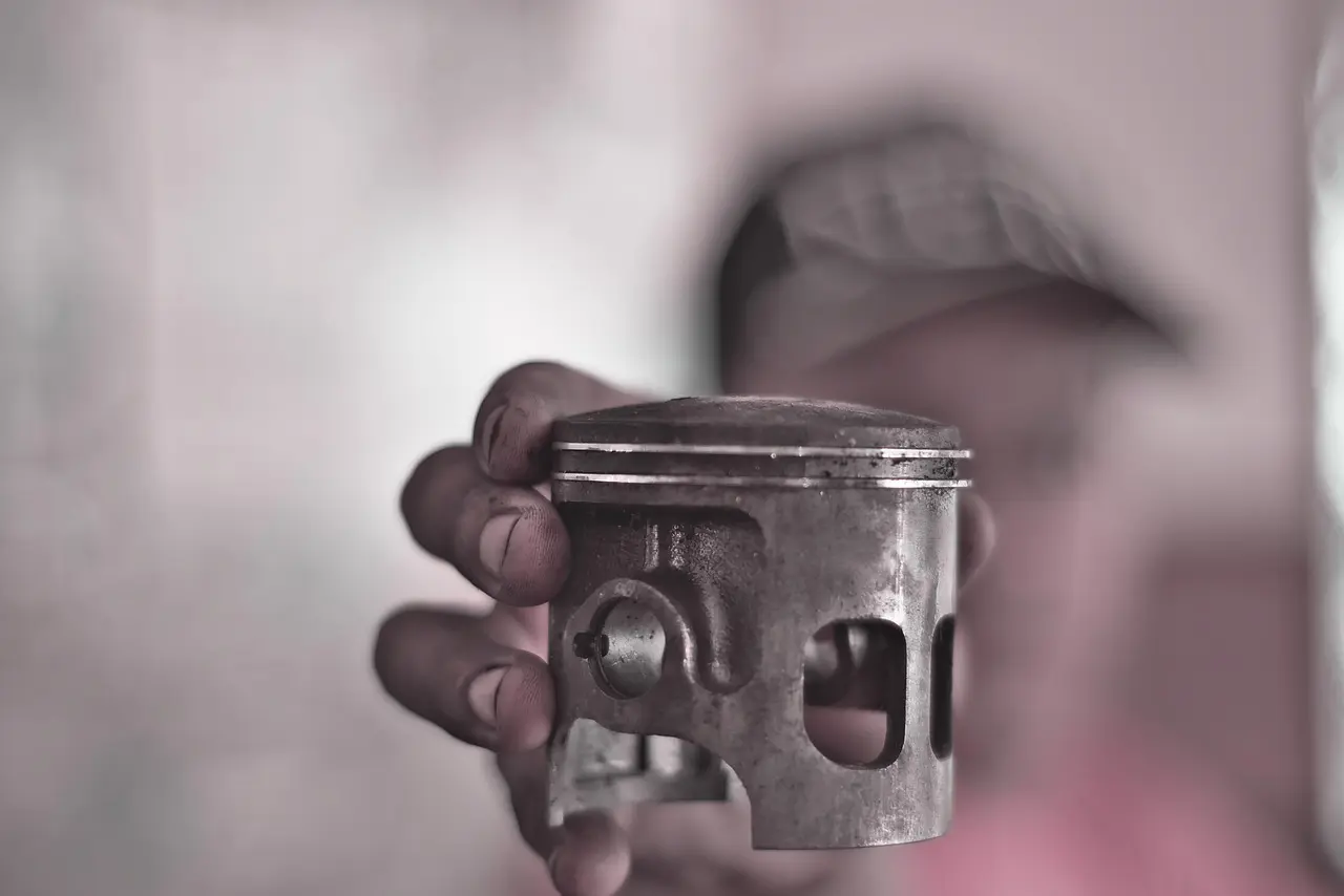 Mechanic's hand holding an engine piston over an open engine in a workshop (generic stock photo, not a Pioneer 1000)
