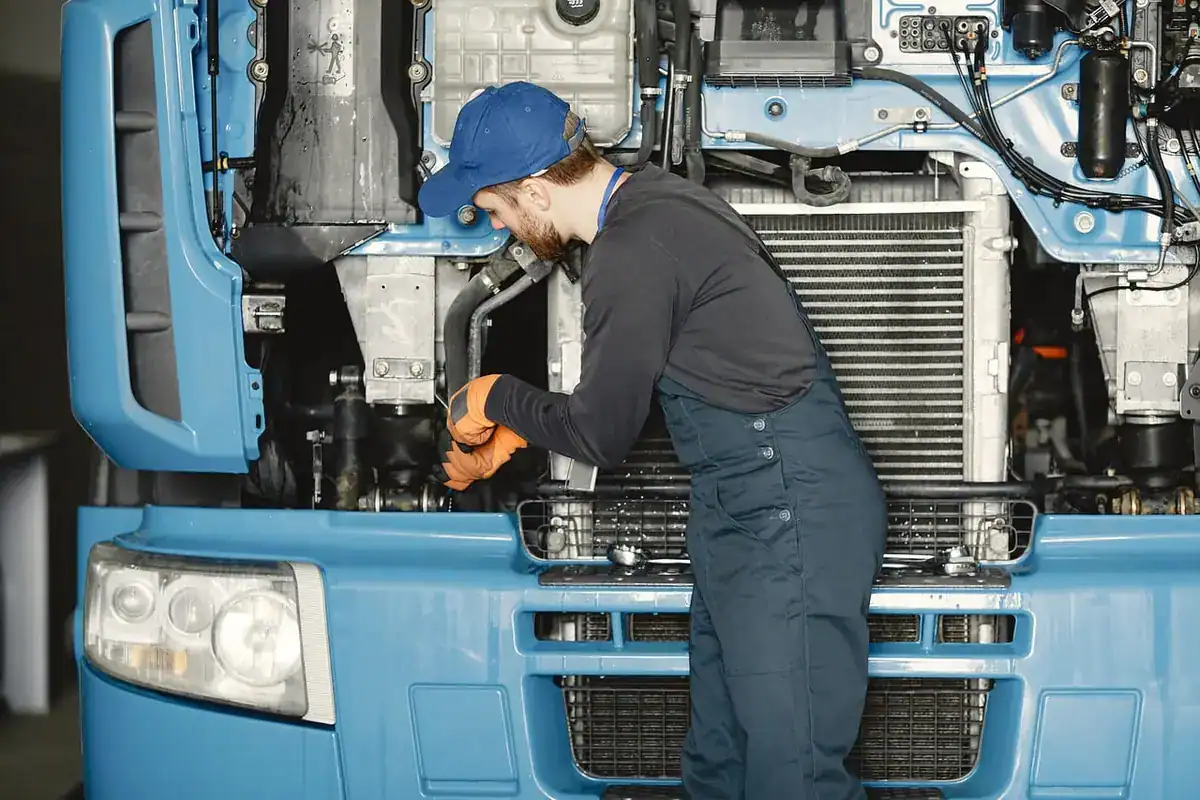Mechanic leaning into the open engine bay of a truck to inspect the radiator and cooling parts