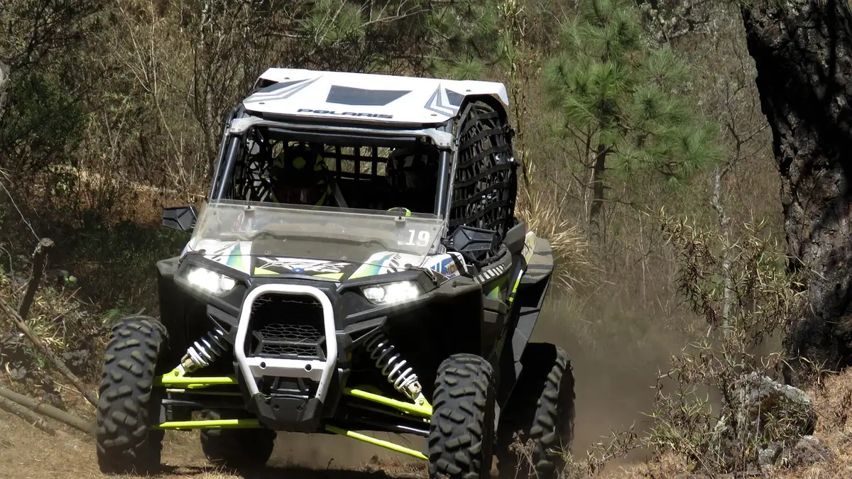 Front of a Polaris RZR XP side-by-side with LED headlights on a dusty forest trail