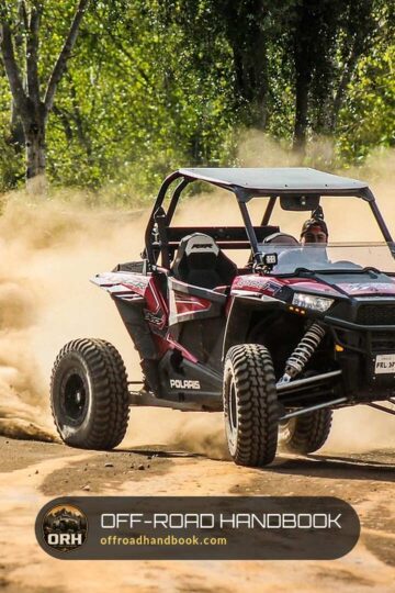 Red and black Polaris RZR sport side-by-side sliding through a dust cloud on a dirt trail in the woods