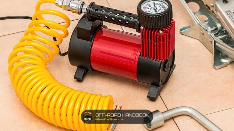 Portable tire air compressor with a pressure gauge and coiled yellow hose — Off-Road Handbook