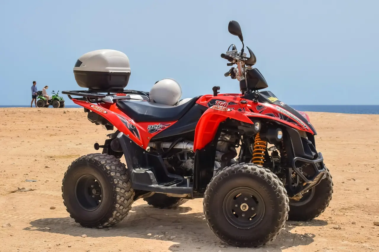 A red four-wheel ATV parked on sandy ground with the sea behind it
