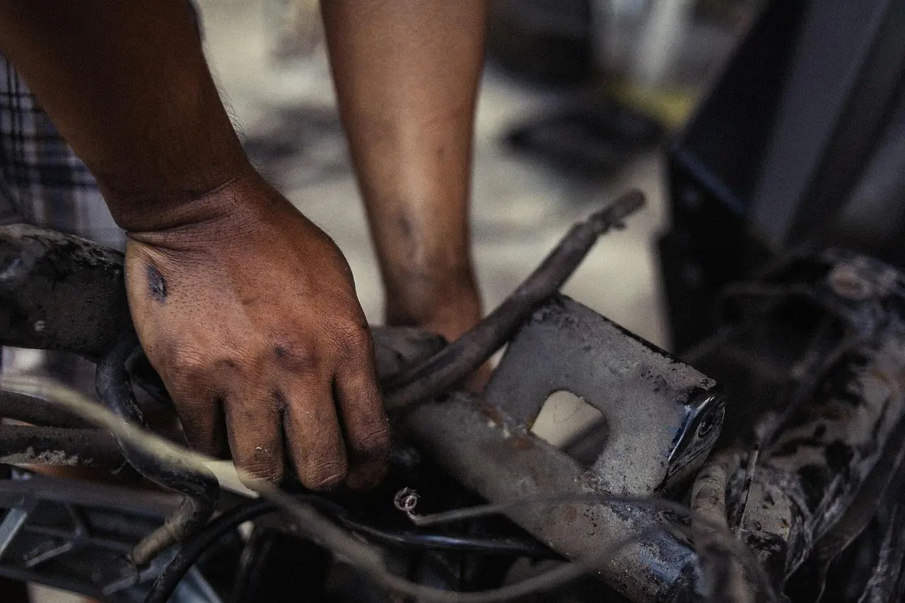 A mechanic’s greasy hand working on wiring and brackets of a muddy off-road machine