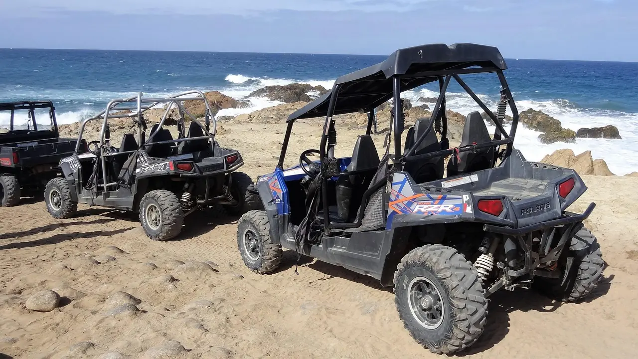 Two side-by-side UTVs parked on a sandy beach near the water