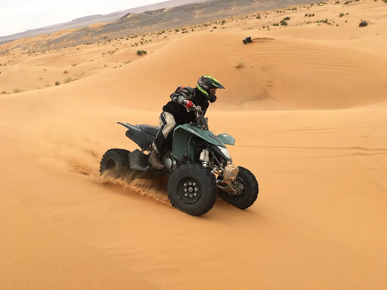 A helmeted rider on a quad bike climbing a sand dune
