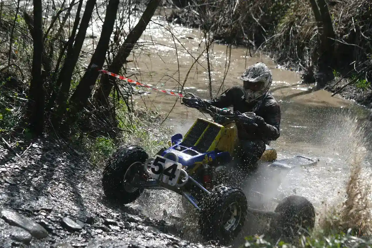 Rider on a racing quad splashing through a muddy stream between trees