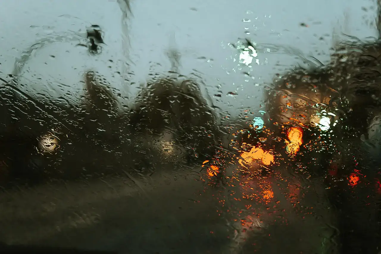 Raindrops running down the glass of a car windshield with blurred brake lights ahead
