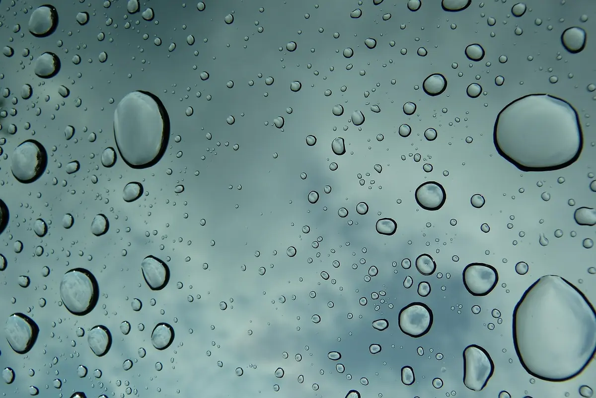 Rain droplets beaded on glass against a cloudy sky