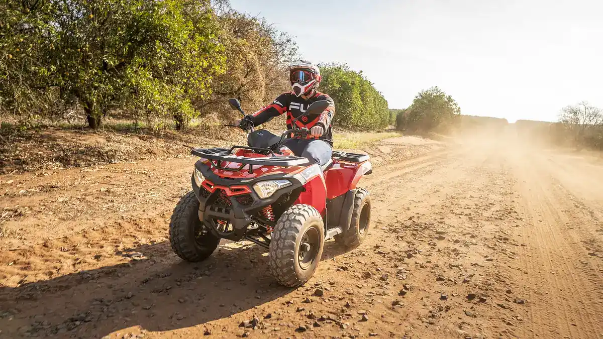 Rider in a helmet on a red ATV riding along a dusty dirt road