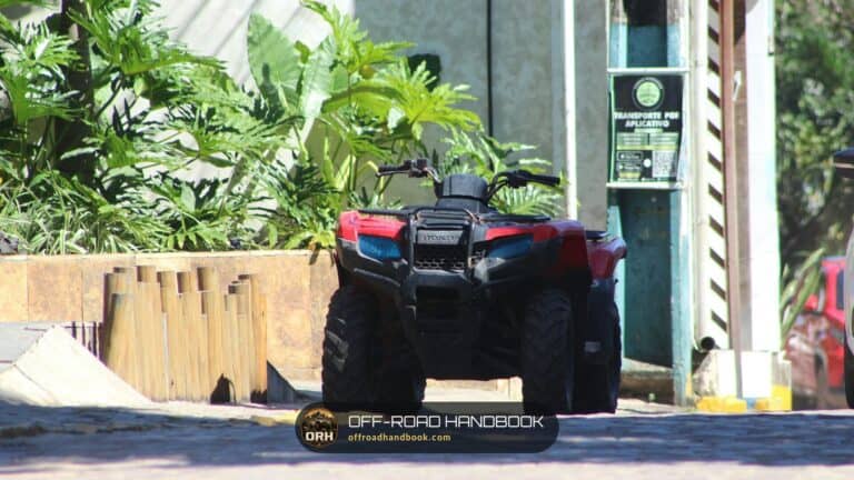 Red and black utility ATV parked on pavement in front of tropical plants
