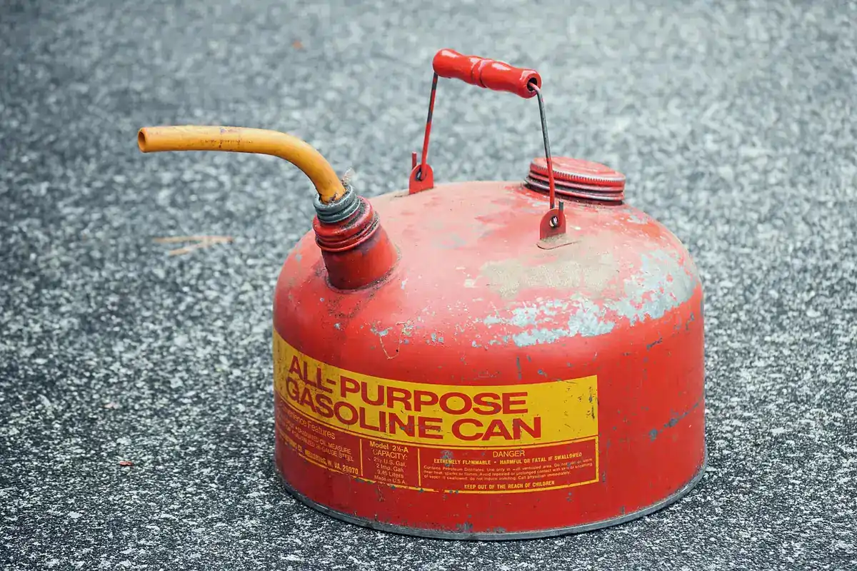Red metal all-purpose gasoline can with a yellow spout sitting on asphalt
