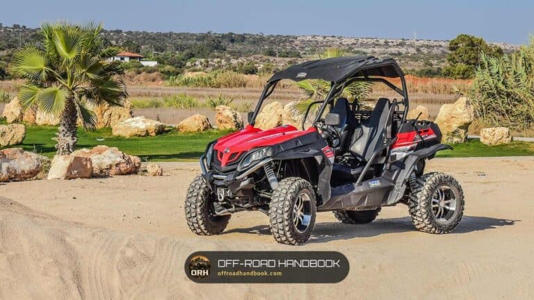 Red side-by-side UTV parked on sand with palm trees behind it — Off-Road Handbook