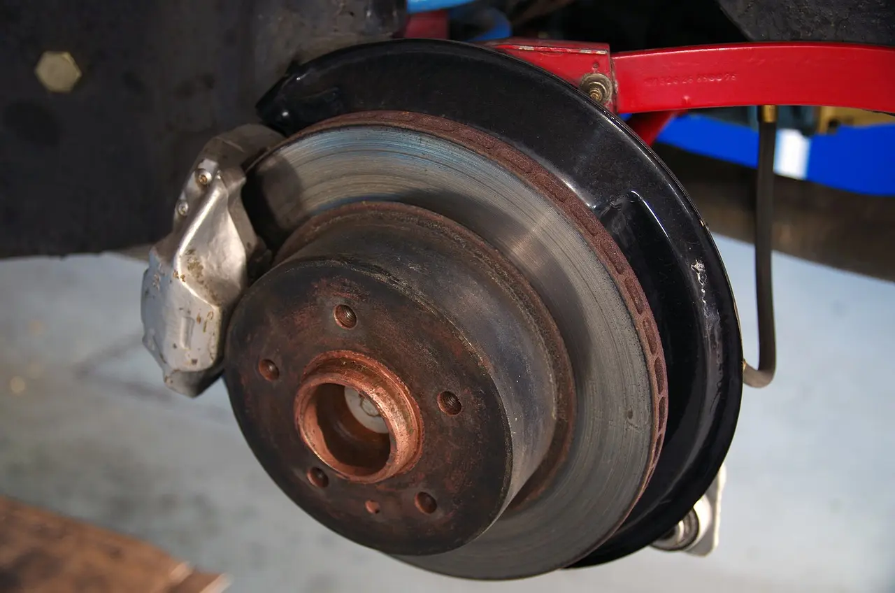 Vehicle brake disc and caliper with the wheel removed, showing surface rust on the rotor hub