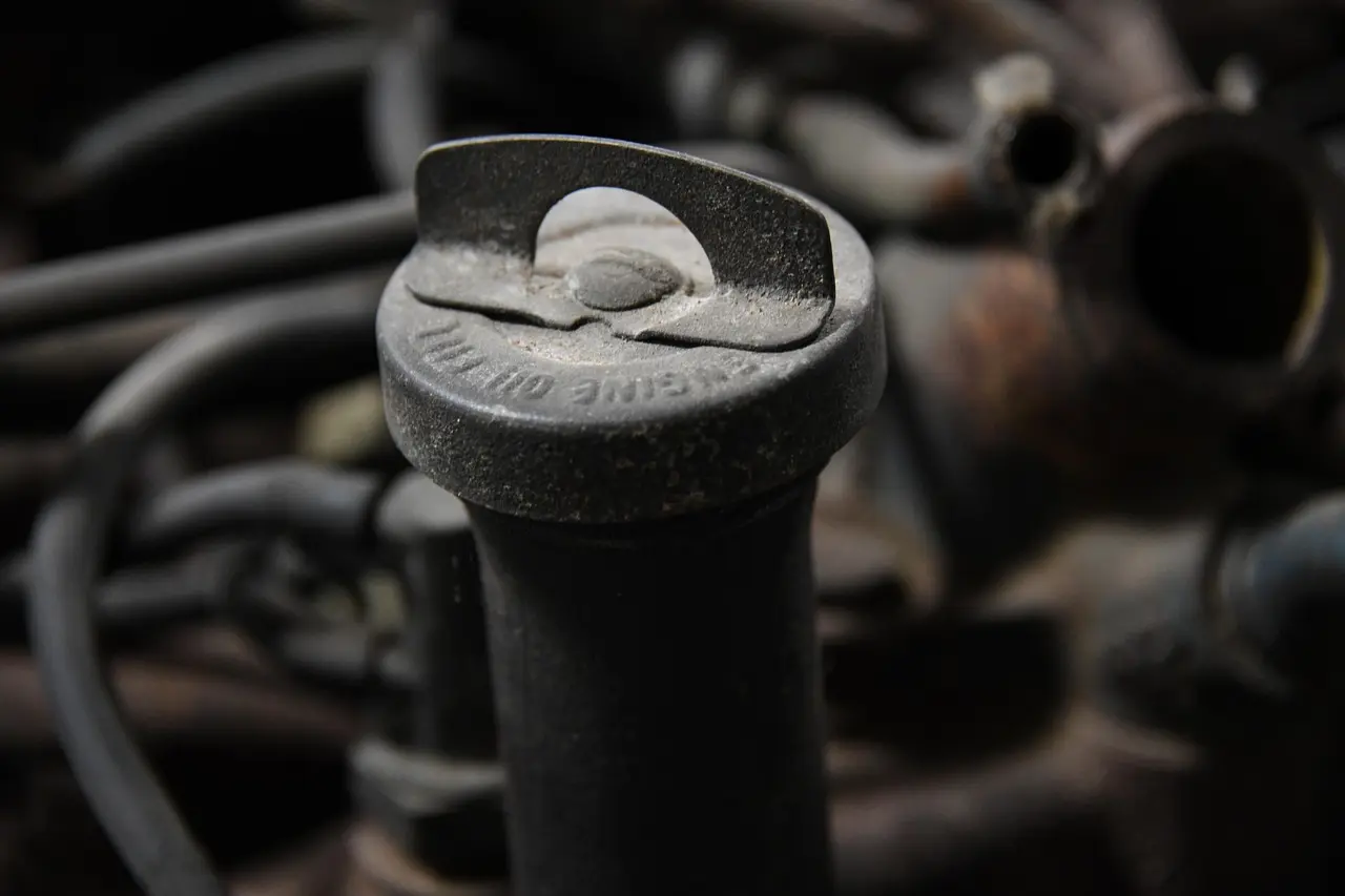 Close-up of a dusty engine oil filler cap on a dipstick-style neck among hoses