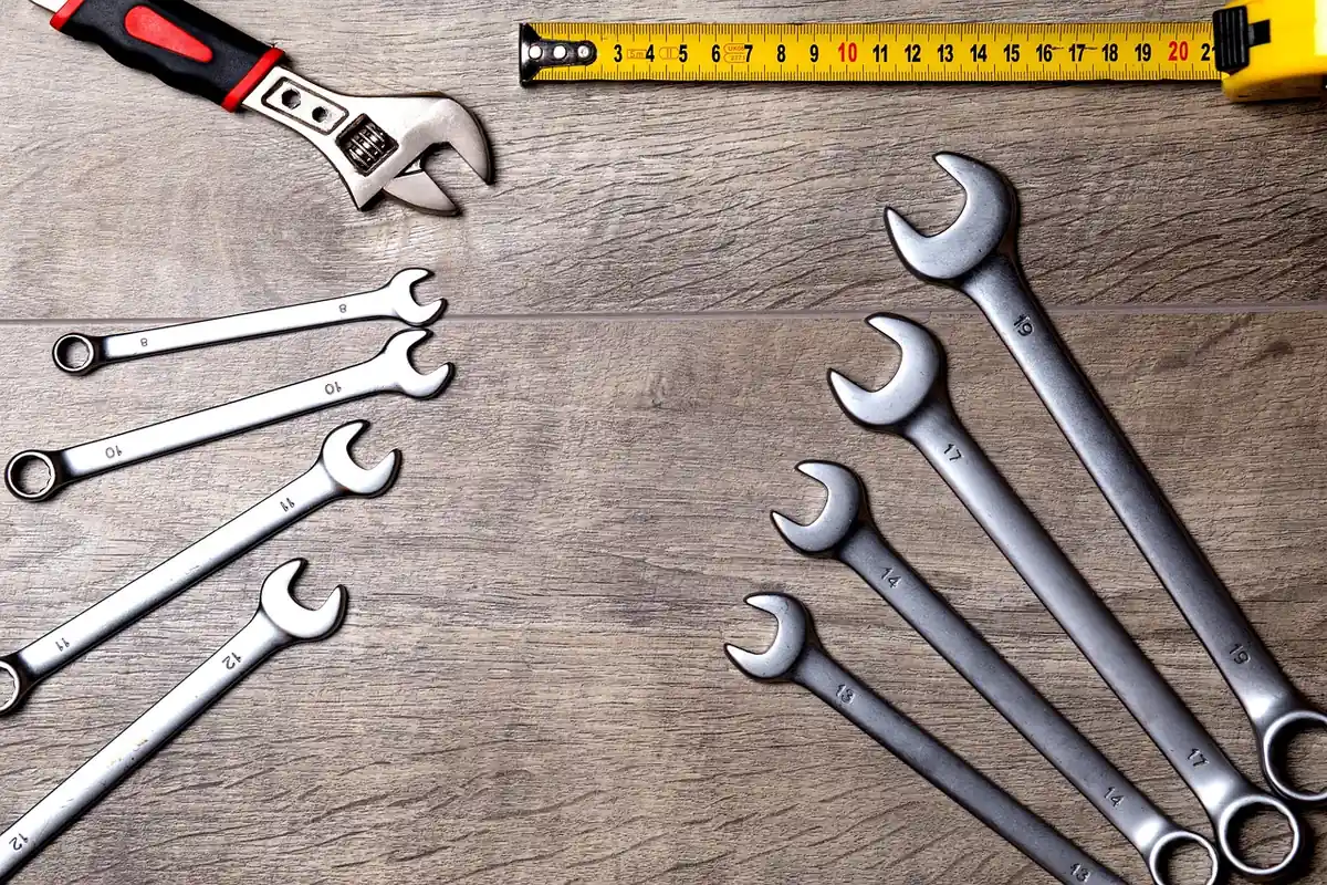 Combination wrenches, an adjustable wrench and a tape measure laid out on a wooden workbench