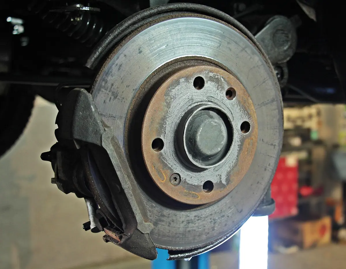 Front brake disc and caliper on a vehicle raised on a lift, showing the rotor face and pad area to inspect (stock photo of a car brake, not a Pro XP)