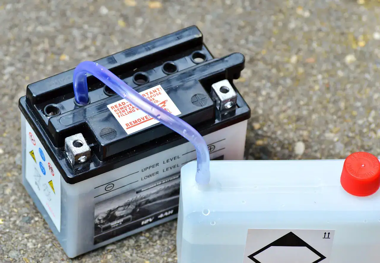 Sealed 12-volt powersports battery with terminals and a bottle of electrolyte on gravel