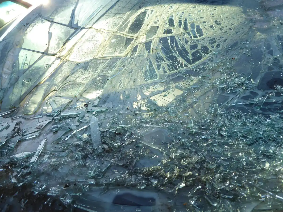 A shattered car windshield with a web of cracks and loose glass fragments